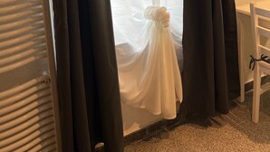 Una habitación con una ventana tapada por cortinas negras, una silla blanca y un radiador.