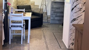 Una sala moderna con un sofá, una mesa de comedor con sillas, una lámpara de pie y un televisor montado en la pared.
