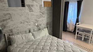 Una cama con colcha, una mesita de noche, una silla y una ventana con cortinas.