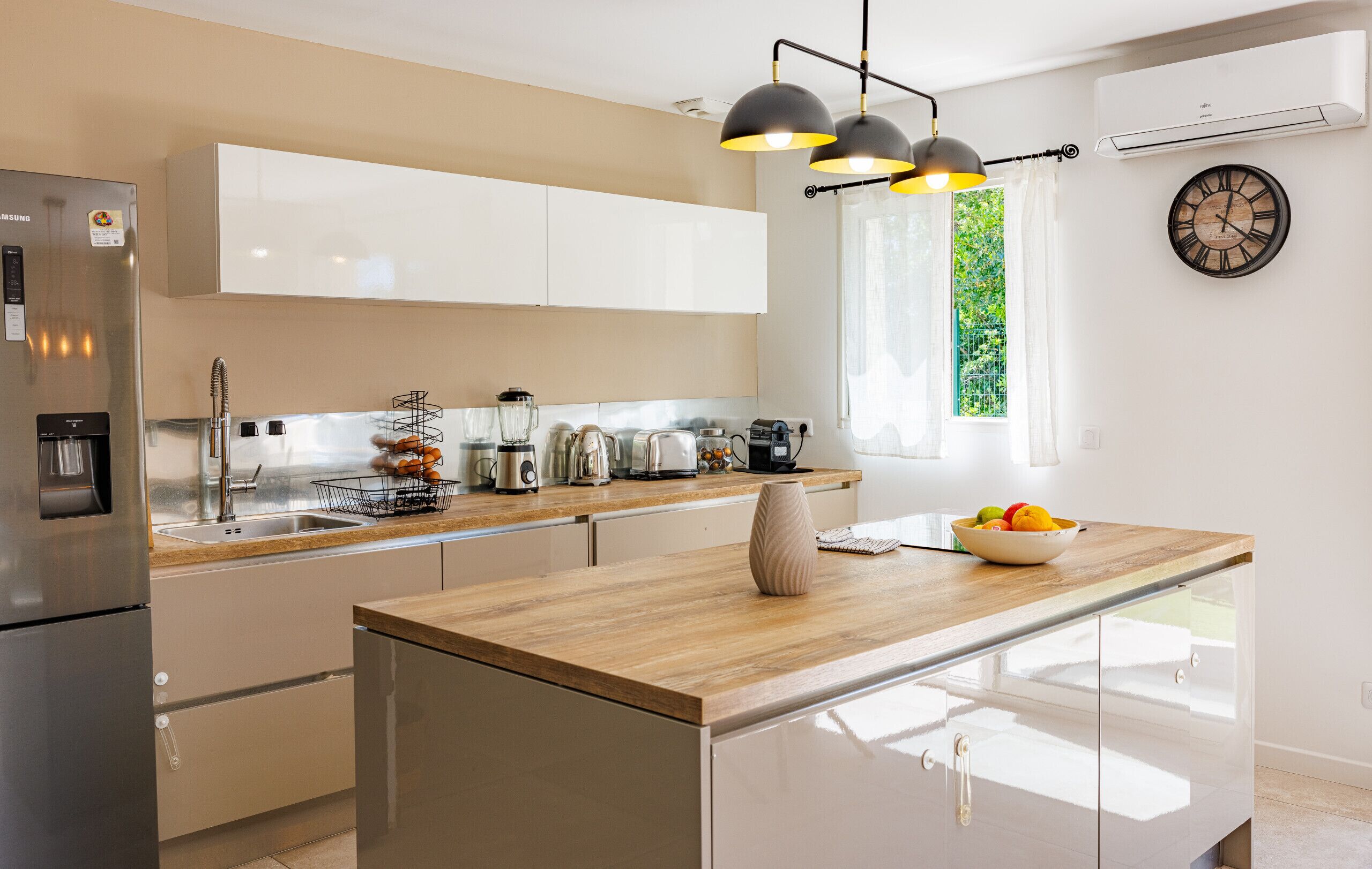 A modern kitchen with a stainless steel refrigerator, a wooden countertop, a built-in oven, and a window with a view of greenery.