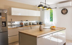 Eine moderne Küche mit Edelstahlkühlschrank, Holzarbeitsplatte, eingebautem Backofen und einem Fenster mit Blick auf Grünflächen.