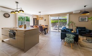 Eine moderne Küche mit Kochinsel, Essbereich mit Stühlen, einer Couch und einer großen Schiebeglastür, die auf eine Terrasse im Freien führt.