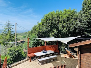 An outdoor patio with a wooden bench, a table, and a shaded area.