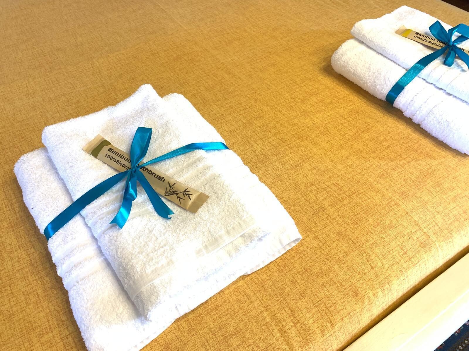 Dos toallas blancas dobladas con cintas y etiquetas azules sobre una superficie de madera.