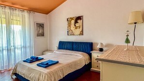 Une chambre à coucher avec un lit, une table de chevet, une lampe, un tableau et une fenêtre avec des rideaux.