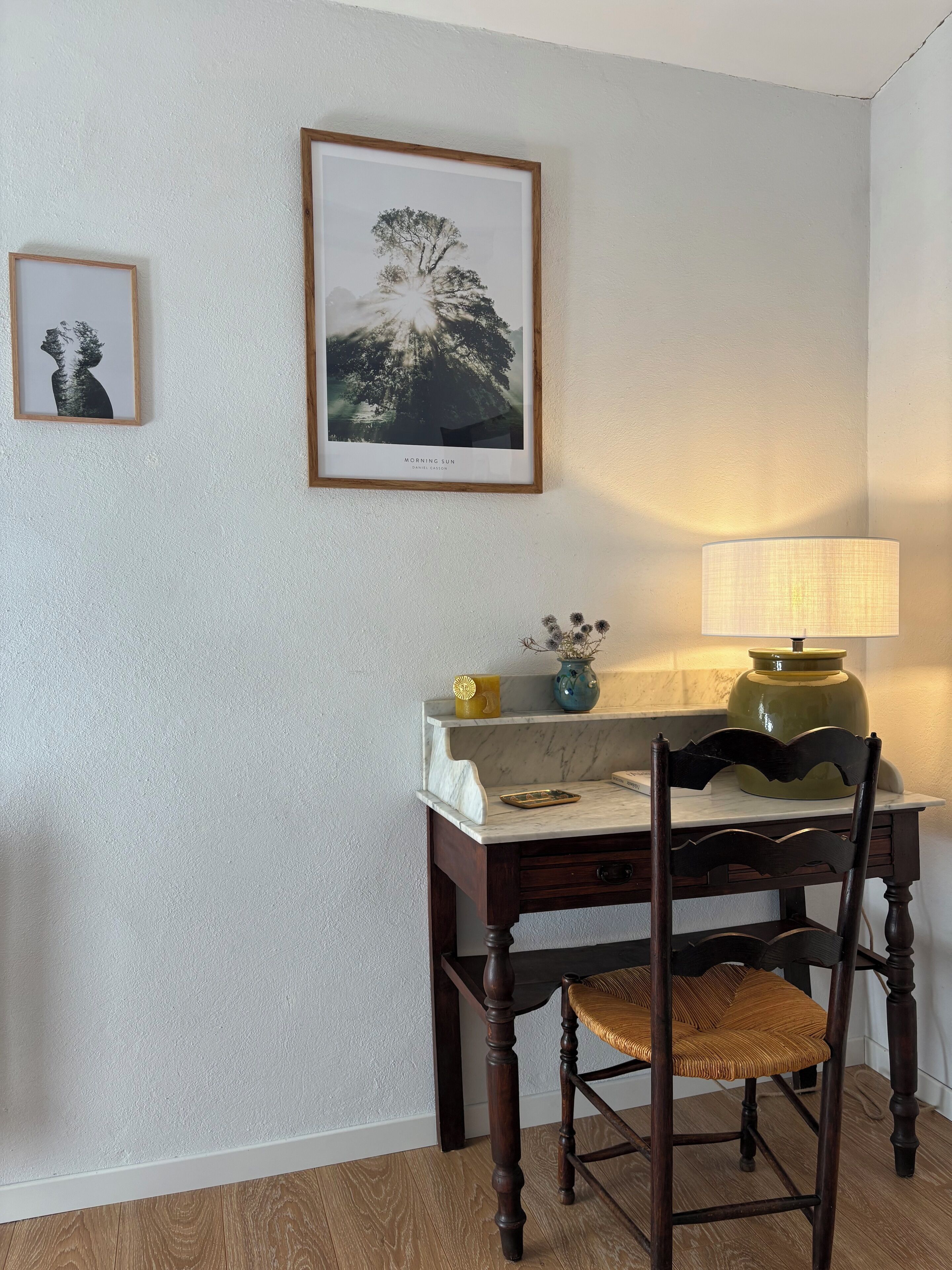 A dining area with a wooden table, a chair, a lamp, and two framed pictures on the wall.