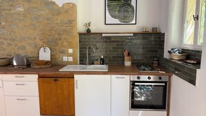A compact kitchen with a stone wall, a sink, a stove, and a dishwasher. - Gîte in the heart of nature (Cavillargues)