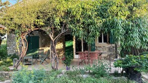 A stone building with a green door, a covered outdoor seating area, and lush greenery. - Gîte in the heart of nature (Cavillargues)