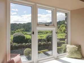 A room with a large window overlooking a green landscape, a stone wall, and a bench. - The Barn at Grasmere (Ambleside)