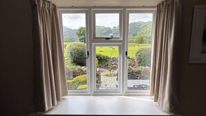 Ein Zimmer mit einem großen Fenster und Blick auf eine grüne Landschaft mit Bäumen und einer Steinmauer.