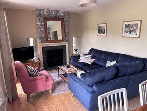 A living room with a blue sofa, a pink chair, a fireplace, and framed pictures on the wall. - The Barn at Grasmere (Ambleside)