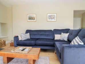 A living room with a blue sofa, two framed pictures on the wall, a wooden coffee table, and a basket. - The Barn at Grasmere (Ambleside)