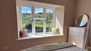 Ein Schlafzimmer mit großem Fenster, einem Bett, einem Schminktisch und einem Spiegel.