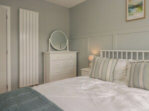 A bedroom with a bed, a dresser with a mirror, a nightstand, and a wall-mounted lamp. - The Barn at Grasmere (Ambleside)