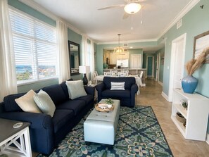 A living room with a sofa, ottoman, and a dining area with a table and chairs. - Azure Resort Luxury, Exceptional Value (Fort Walton Beach)