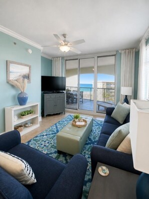 A living room with a sofa, a coffee table, a TV, and a balcony with a view. - Azure Resort Luxury, Exceptional Value (Fort Walton Beach)