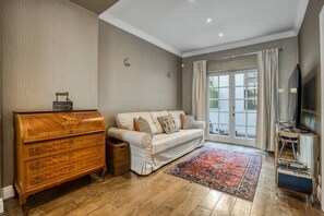 Ein Wohnzimmer mit einem hölzernen Kommode, einem Sofa, einem Fernseher und einem großen Fenster.