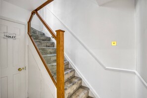 Eine Treppe mit einer Holzhandläufe, eine Tür mit der Aufschrift 'TOILET' und ein Lichtschalter an der Wand.