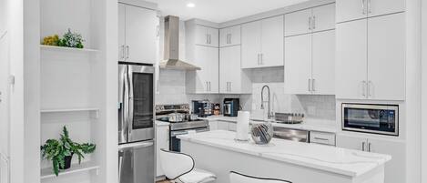 Fully equipped modern kitchen with sleek white cabinets, stainless steel appliances, and a spacious island—perfect for home-cooked meals during your stay.