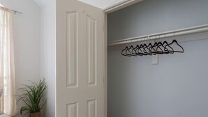 Ein Zimmer mit weißer Tür, einem Blumentopf und einem Kleiderständer mit Kleiderbügeln.
