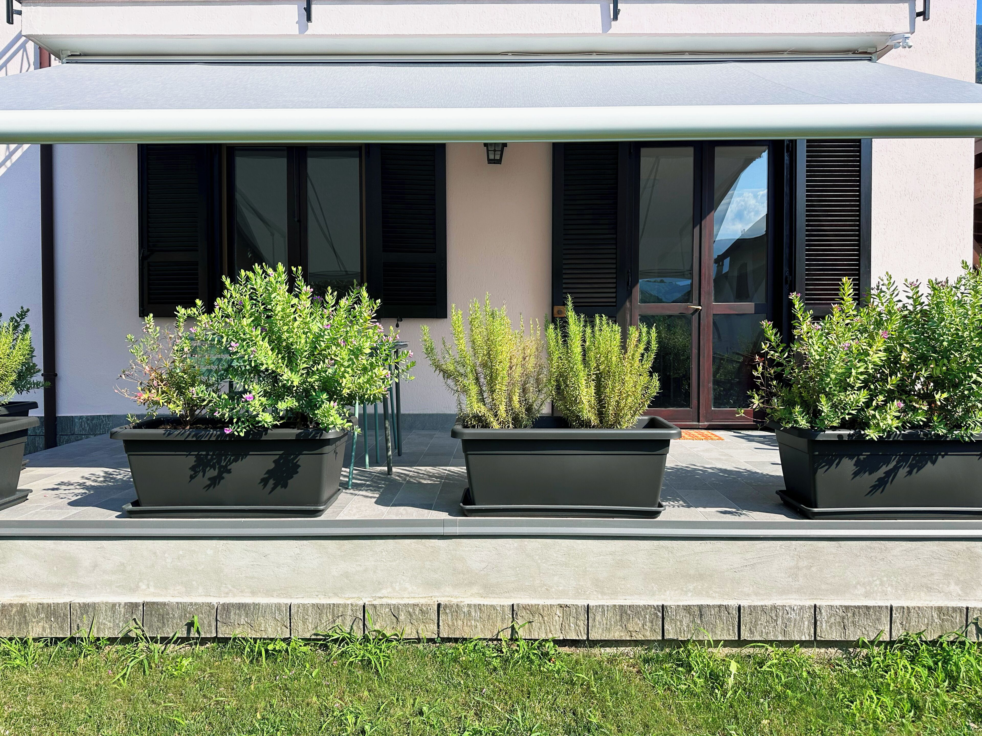 A modern building with three large planters on the ground floor, a covered walkway, and a door with glass panels.