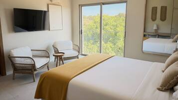 Habitación de hotel con cama, dos sillas, una mesita, televisor y un ventanal con vistas.