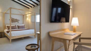 A room with a four-poster bed, a flat-screen TV, a wooden desk, and a small round table with glasses.