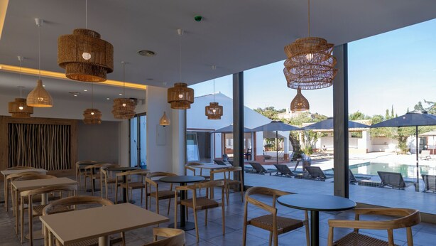 En restaurang med uteservering med utsikt över en pool, inredd med möbler i rotting och hängande lampor.