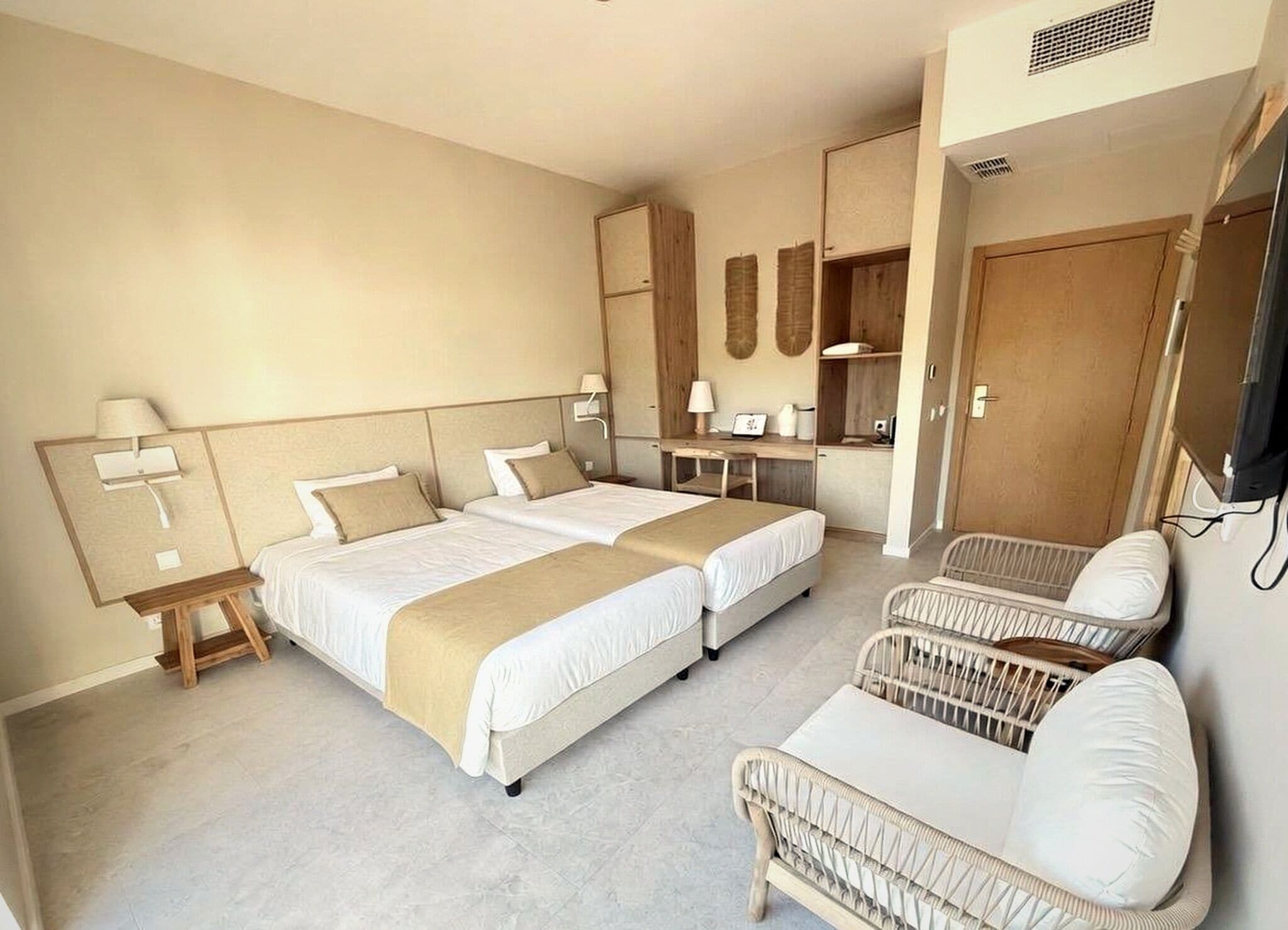 A hotel room with two beds, a desk, a chair, and a television.