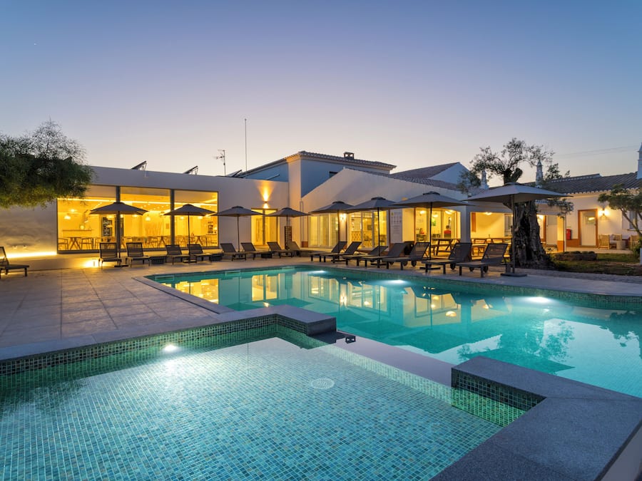 Una piscina con sillones de descanso y sombrillas, rodeada de edificios con amplias ventanas y terrazas.