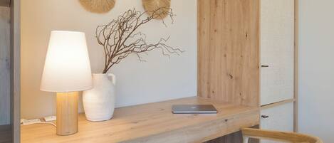 A wooden desk with a white lamp, a white vase with branches, and a laptop.