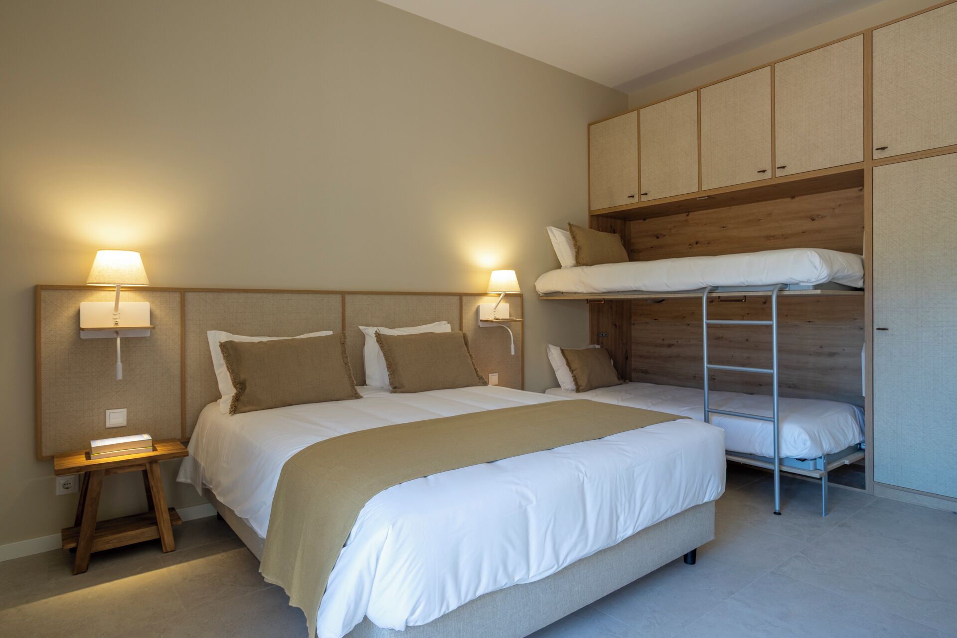 A bedroom with a bunk bed, a single bed, bedside lamps, and a small table.