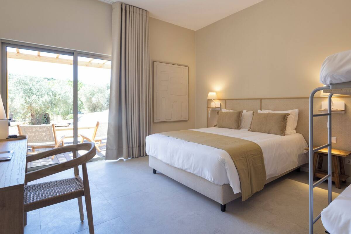 Habitación de hotel con cama, escritorio con silla, literas y vista al exterior.