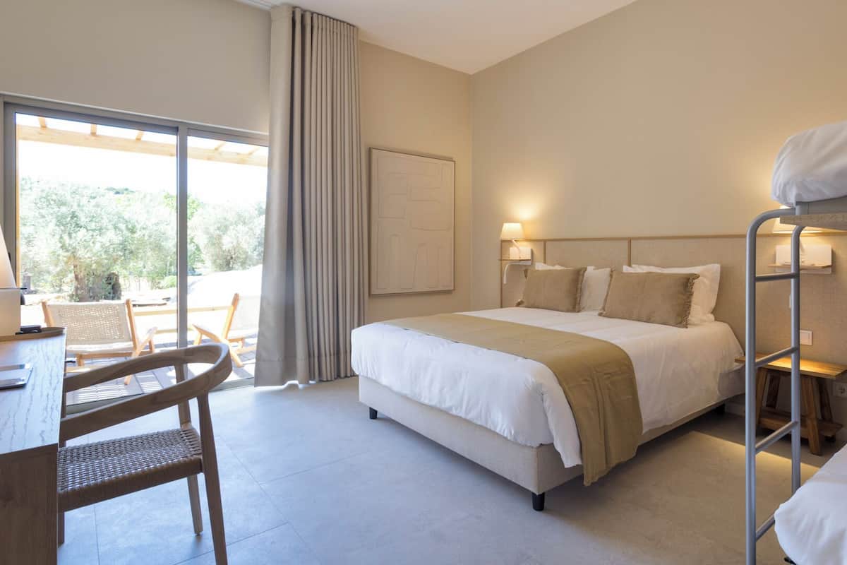 Ein Hotelzimmer mit Bett, Schreibtisch mit Stuhl, Stockbett und Blick ins Freie.