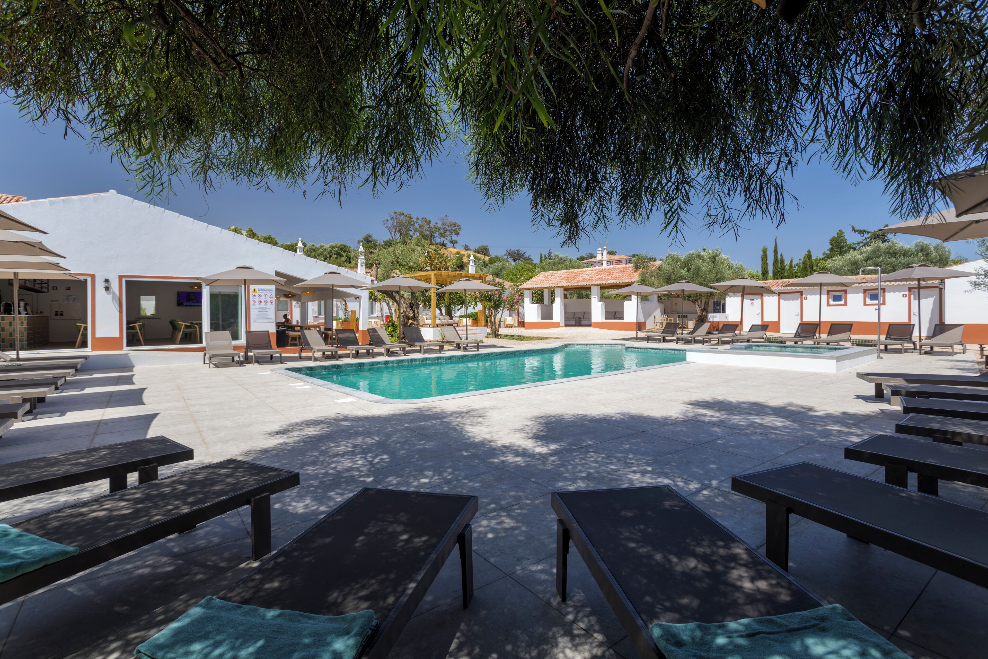 A poolside area with lounge chairs, a swimming pool, and a building with a tiled roof.