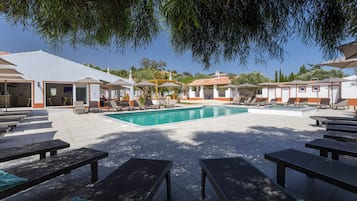 A poolside area with lounge chairs, a swimming pool, and a building with a tiled roof.