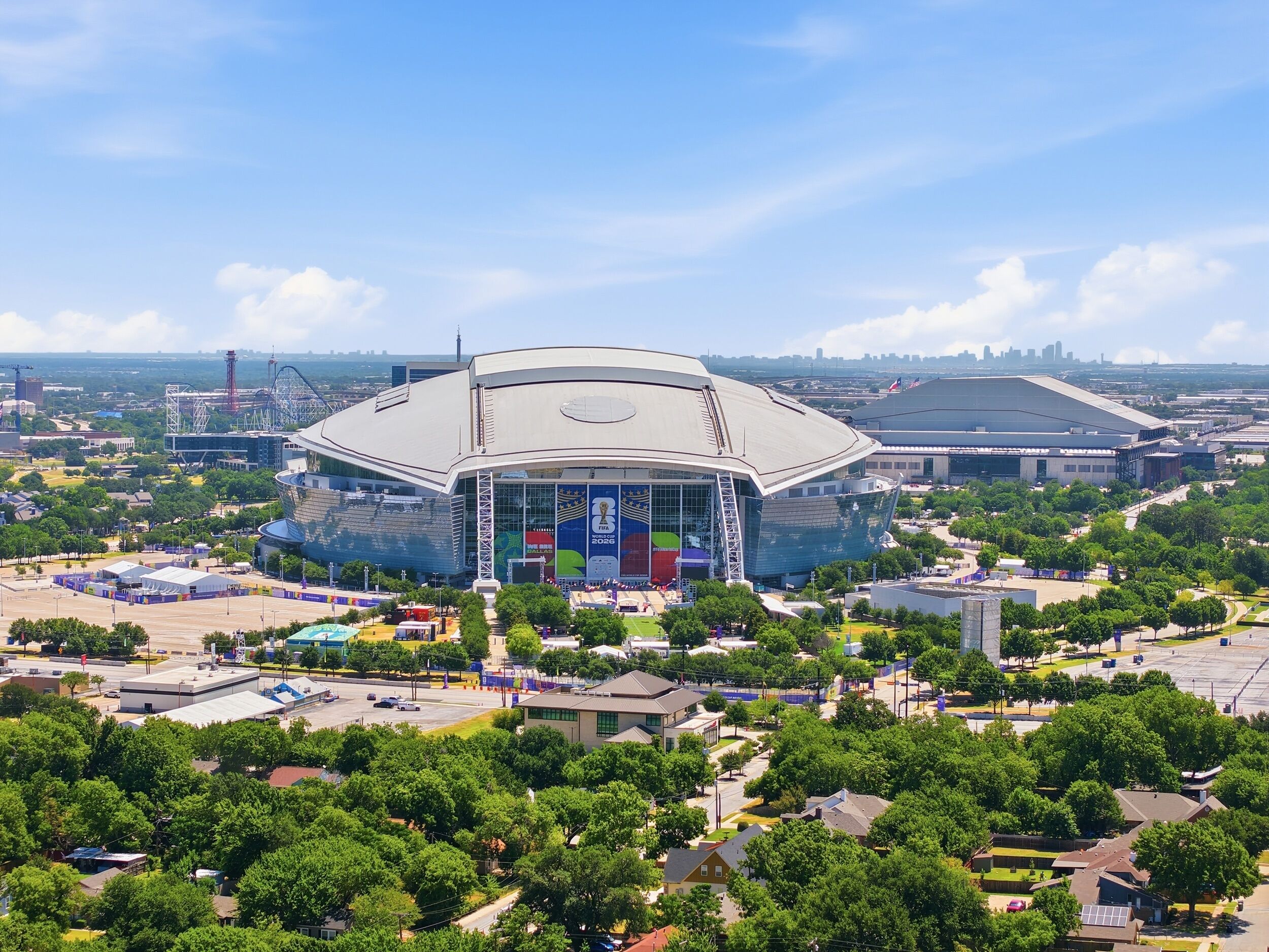 A large stadium with a modern design, surrounded by greenery and urban buildings.