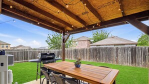 Un patio al aire libre con una mesa y sillas de madera, una parrilla y una guirnalda de luces.