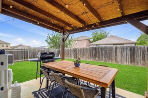 An outdoor patio with a wooden table and chairs, a grill, and a string of lights. - Vibrant Stay Near SeaWorld w Patio & BBQ | Pets OK (San Antonio)
