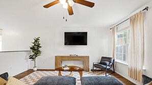 Una sala de estar con un sofá, una mesa de centro, una chimenea, un televisor y un ventilador de techo.