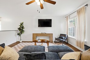A living room with a sofa set, a coffee table, a fireplace, a television, and a ceiling fan. - Vibrant Stay Near SeaWorld w Patio & BBQ | Pets OK (San Antonio)