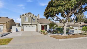 A residential street with houses, a driveway, and a tree.