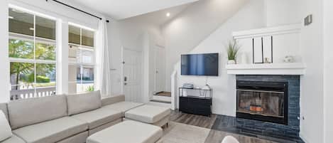 Un salon moderne doté d’un canapé d’angle, d’un téléviseur à écran plat, d’une cheminée et d’un escalier menant à un niveau supérieur.
