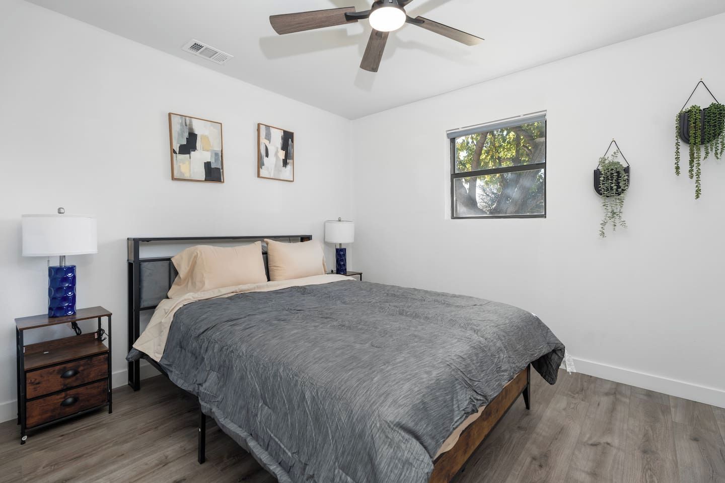 A bedroom with a bed, two bedside tables, a ceiling fan, a window, and wall art.