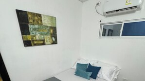 Ein Einzelbett mit grauem Matratze, weißen und türkis-farbenen Kissen sowie einer blauen Bank.