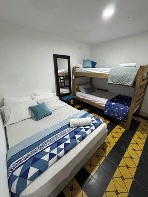 Ein Zimmer mit einem Einzelbett, einem Etagenbett, einem Spiegel und einem Fliesenboden.