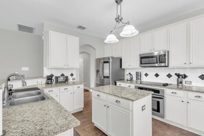 Une cuisine moderne avec des meubles blancs, des comptoirs en granit, des appareils électroménagers en acier inoxydable et un îlot central.