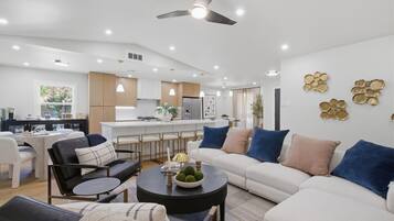 A modern living room with a sofa, coffee table, and chairs. There is a kitchen area with a refrigerator and cabinets.