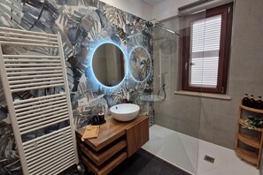 Een moderne badkamer met een grote spiegel, een wit wastafel, een houten meubel en een douchehoek.