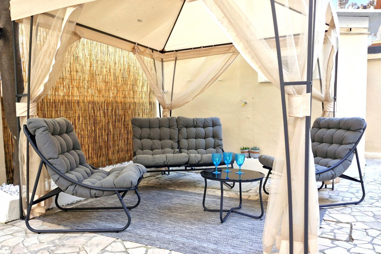 Un espacio de estar al aire libre cubierto con sillas acolchadas y una mesa, un fondo de bambú y un toldo blanco.
